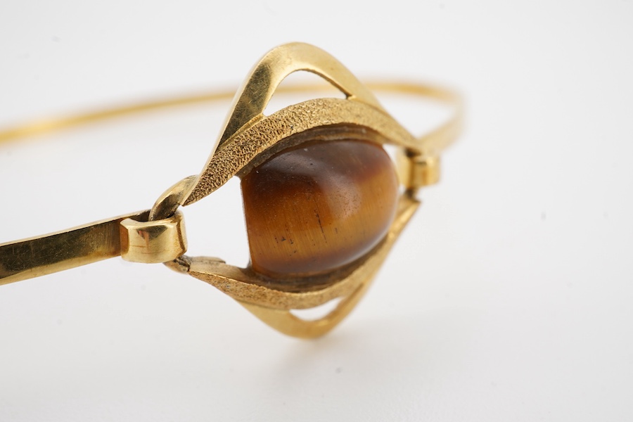 A modern continental 18k and single stone tiger's eye quartz set bangle, gross weight 7 grams.